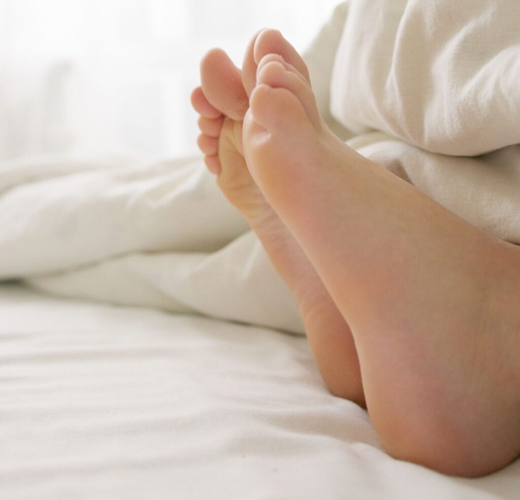 Close-up of bare feet under a white blanket in a serene bedroom setting.